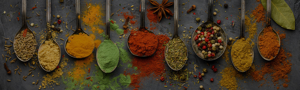 image of colorful ground up spices in powder form, in separate spoons right next to each other on a concrete background