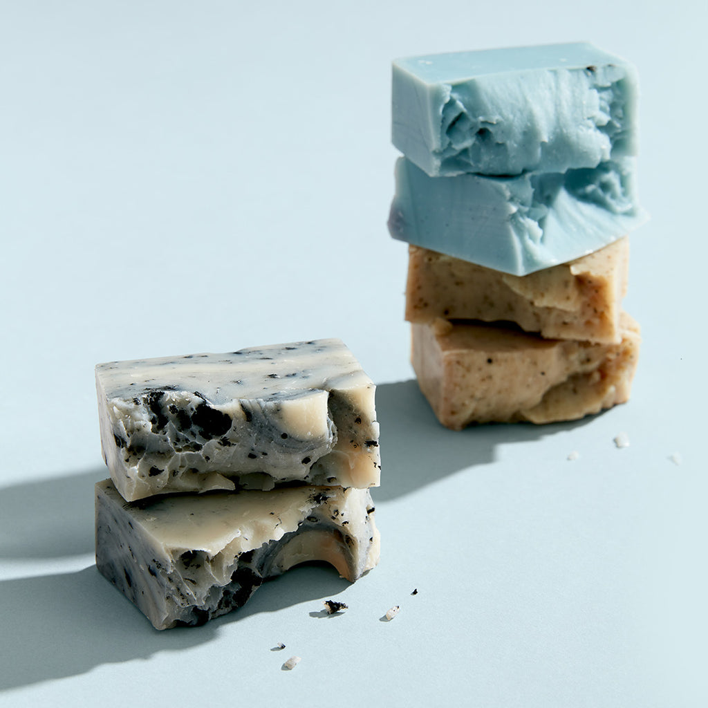 Image of three unboxed soaps that have been broken in half, against a light blue background