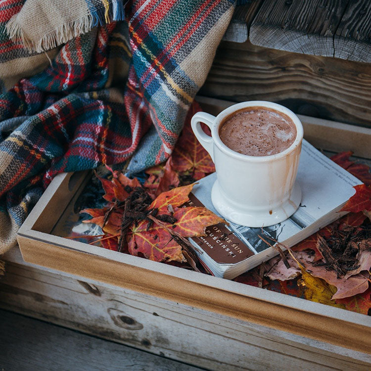 image of a mug of coffee sitting on a small wooden tray covered with fall colored leaves with a plaid blanket next to it