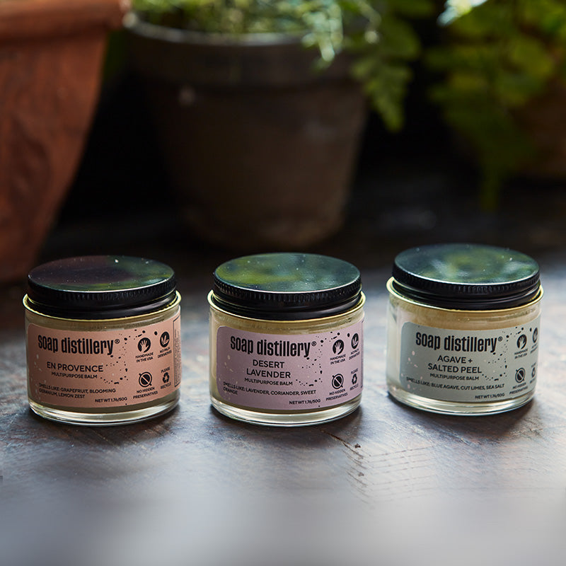 three multipurpose balms in glass packaging with a aluminum cap with potted plants in the background