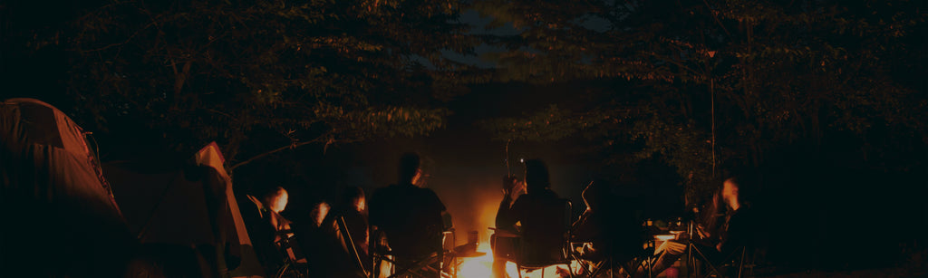 Image of people camping and sitting around a campfire at night.