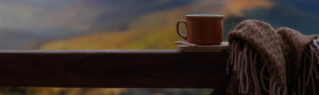 image of a mug and blanket sitting on a narrow shelf outside with a blurred view of the mountains with fall leaves in the background