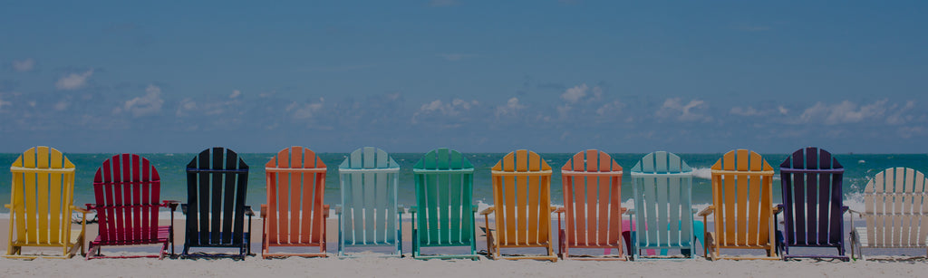image of colorful beach chairs outside in white sand on front of the ocean with a blue sky in the background