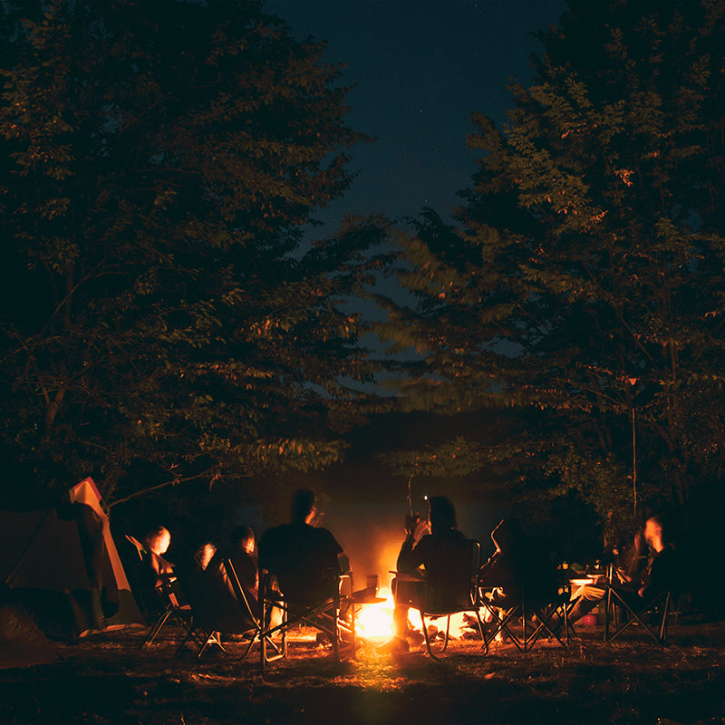 Image of people camping and sitting around a campfire at night.