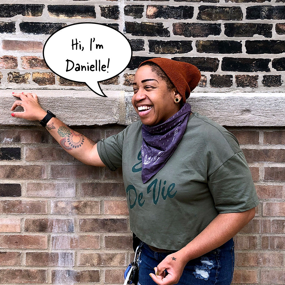 Image of Danielle Martin, the owner and founder of Soap Distillery, standing outside near a brick wall, laughing, with the words "Hi, I'm Danielle!" in a comic style speech bubble