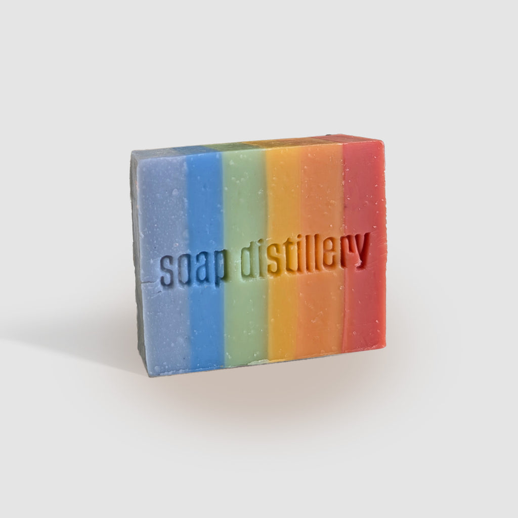 rainbow colored bar soap on its side with the Soap Distillery logo stamped onto it against a light grey background