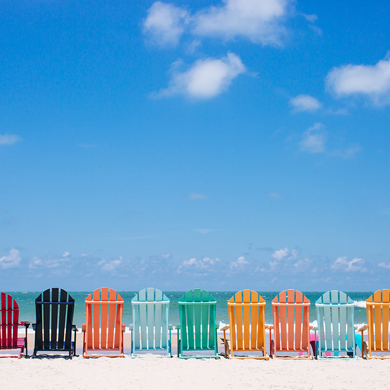 image of colorful beach chairs outside in white sand on front of the ocean with a blue sky in the background