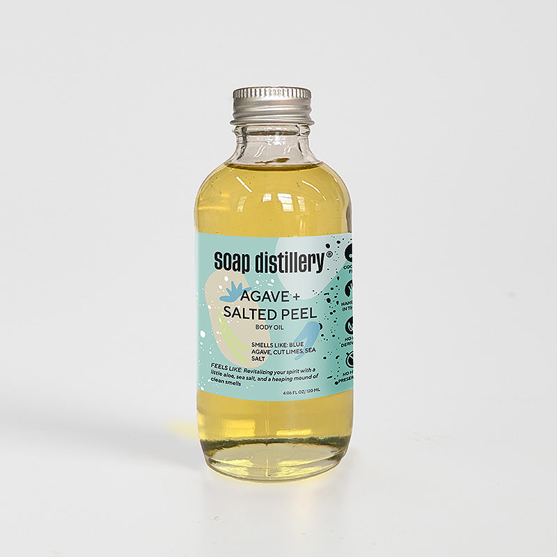 golden body oil in glass bottle with silver cap and aqua colored label