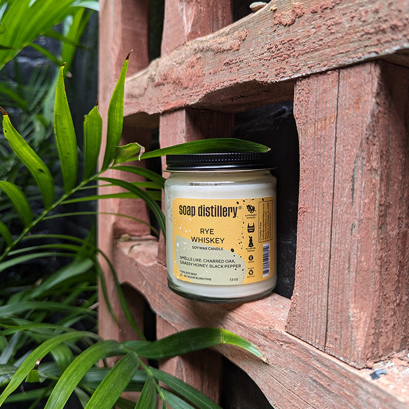 image of rye whiskey candle sitting in a deep wooden trellis outside near plants