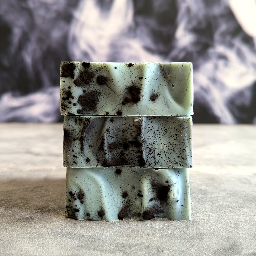 close up of green and black swirled bar soap on a grey surface with a smoky background