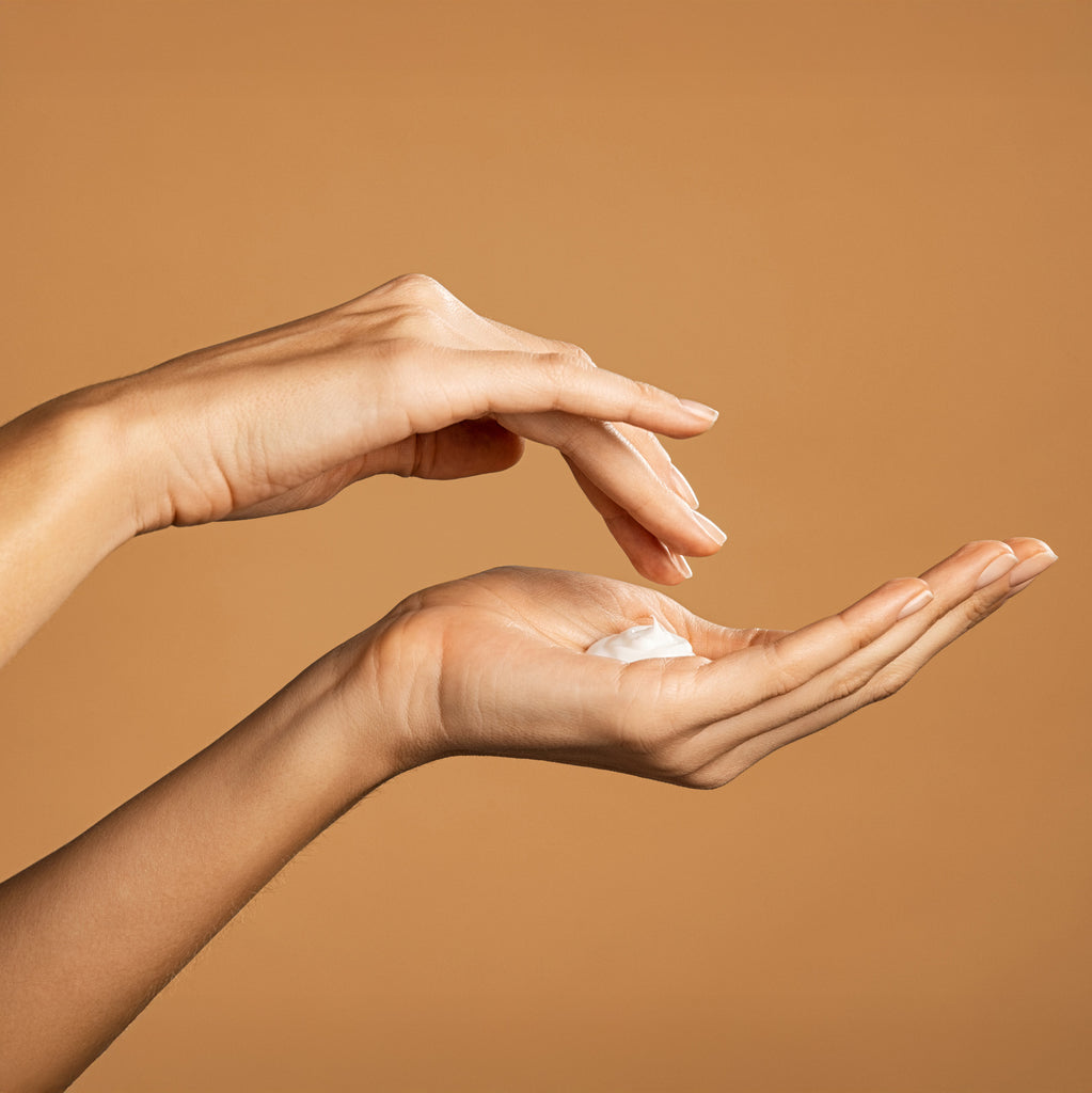 Two hands holding a small amount of cream against a brown background
