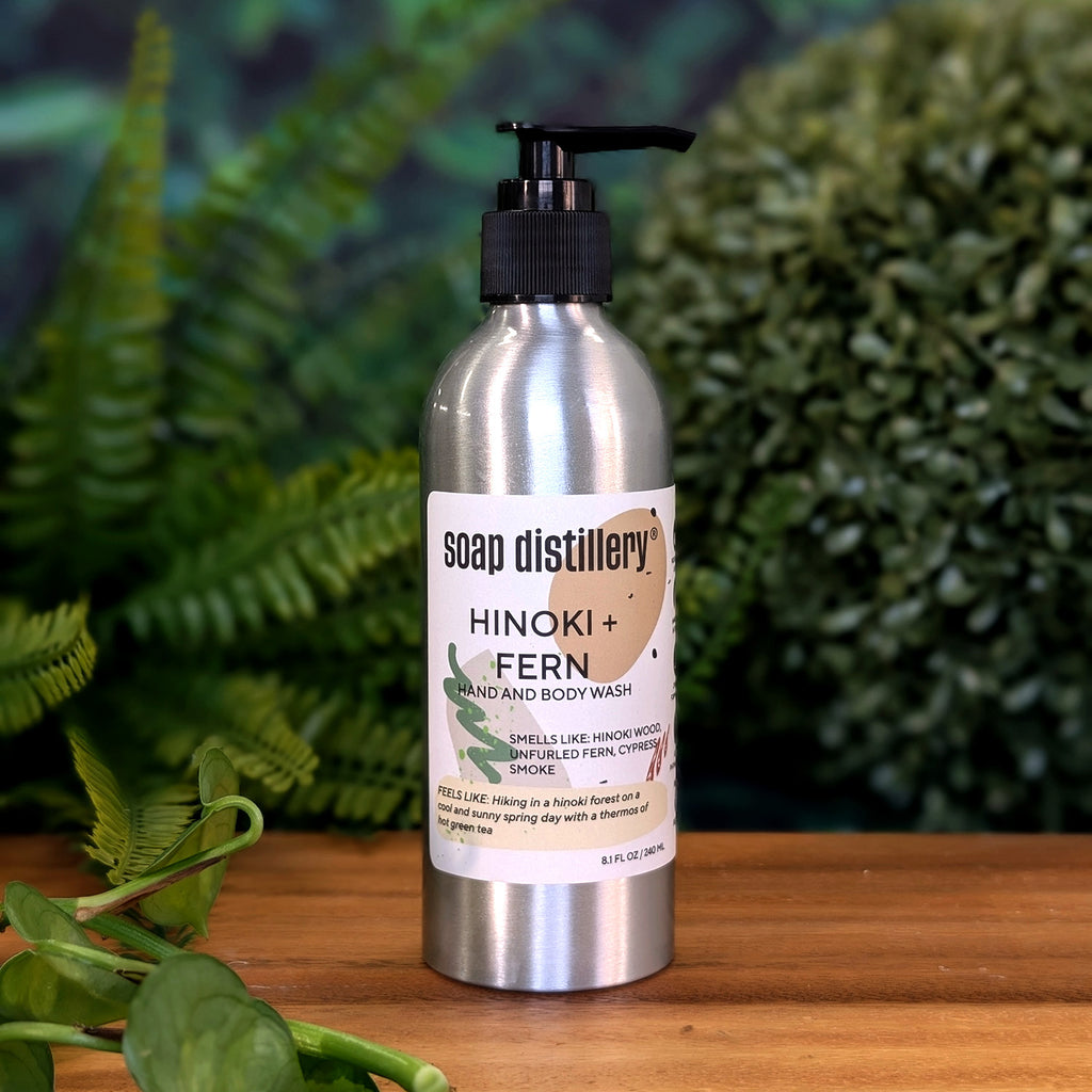 hand and body was in a silver aluminum bottle with black pump and tan colored label on a wooden surface with plants in the background