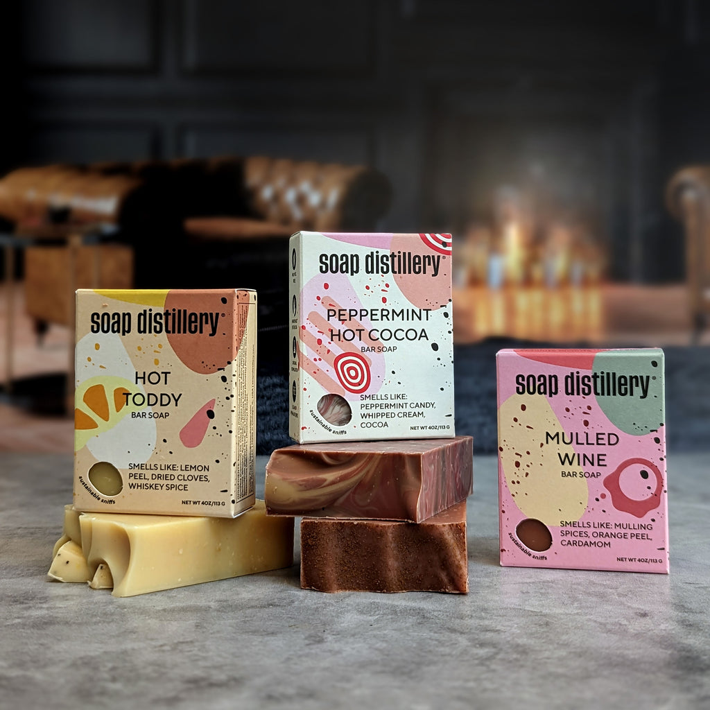 hot toddy, peppermint hot cocoa, and mulled wine bar soaps in colorful packaging against a blurred lifestyle background