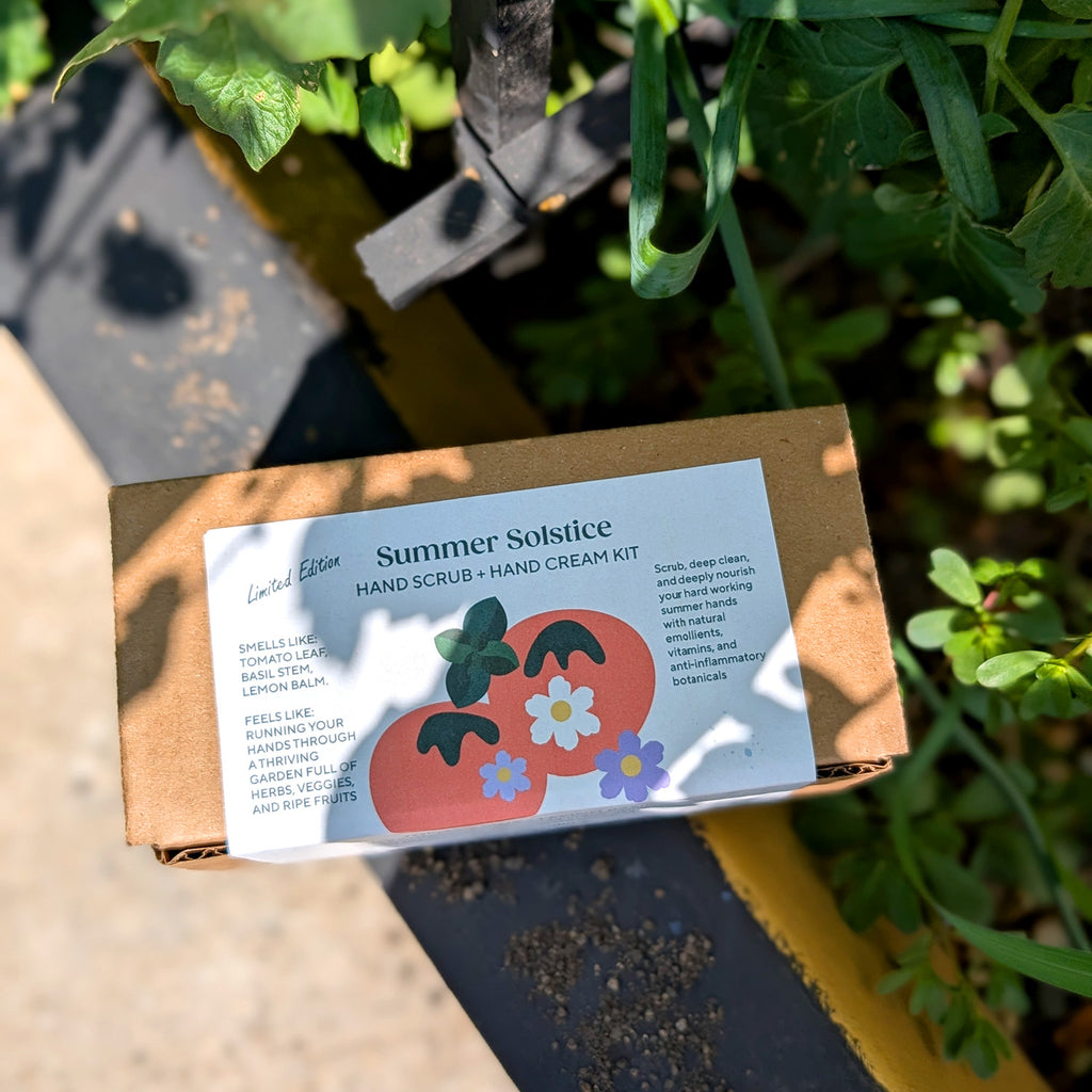 Summer Solstice hand scrub and hand cream kit packaging on a garden bench with plants in the background