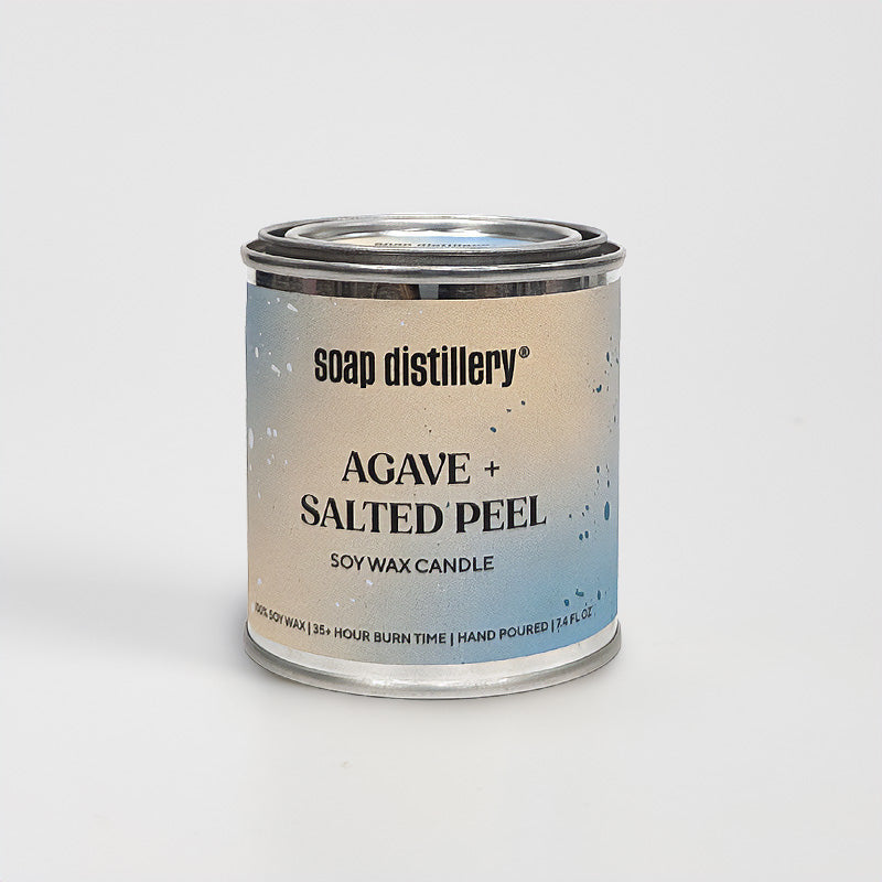 candle in a small paint can with a colorful label against a grey background