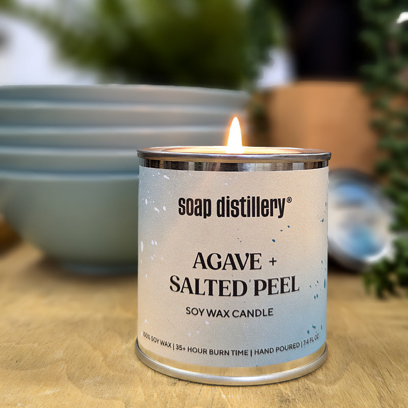 candle in a small paint can with a colorful label on a wooden surface and depth of field background