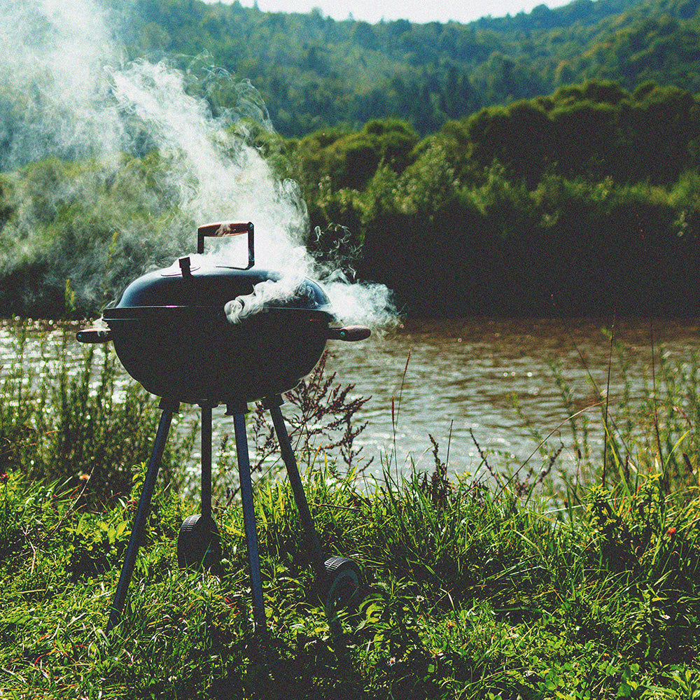 a smoky charcoal grill against a green and lush background by a river setting