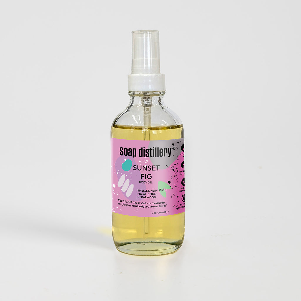 golden body oil in glass bottle with white pump top and magenta colored label against a light grey background. Scent is called sunset fig