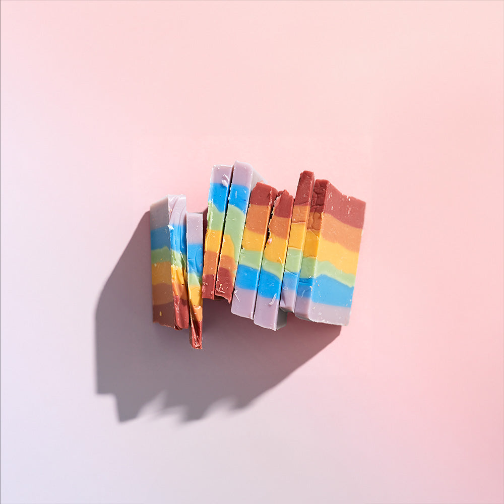 slices of rainbow bar soap leaning on each other on a pink background flat lay