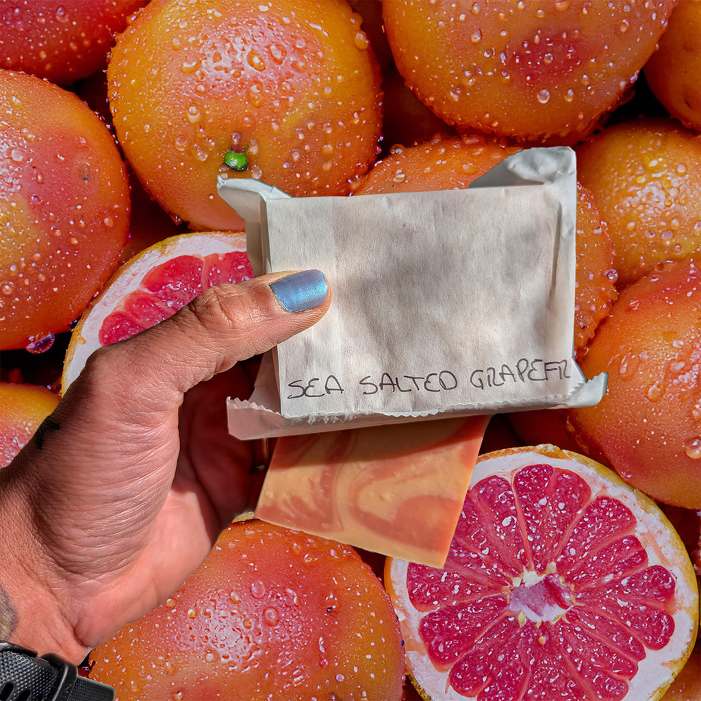 hand holding wrapped soap above grapefruits covered with water droplets