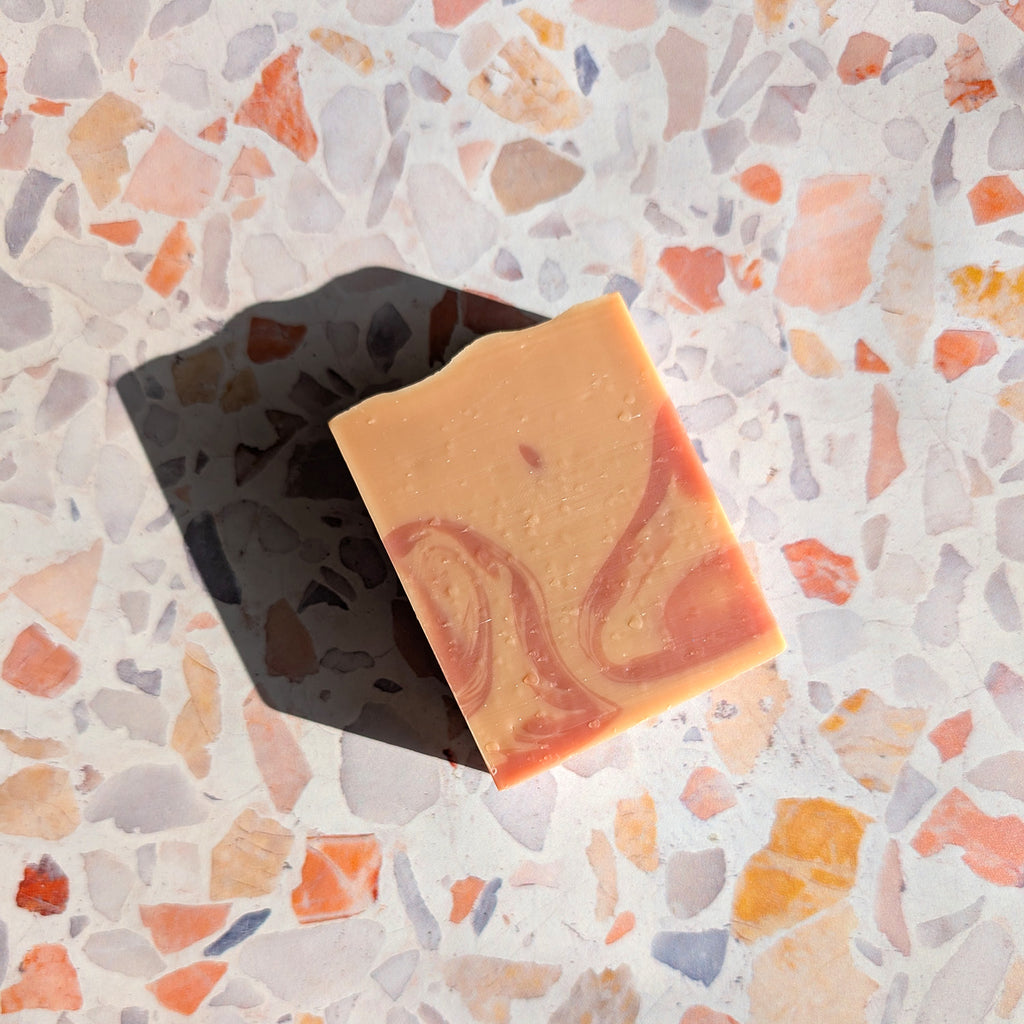 aerial shot of package free peach colored bar soap with a dark peach swirl and a strong shadow