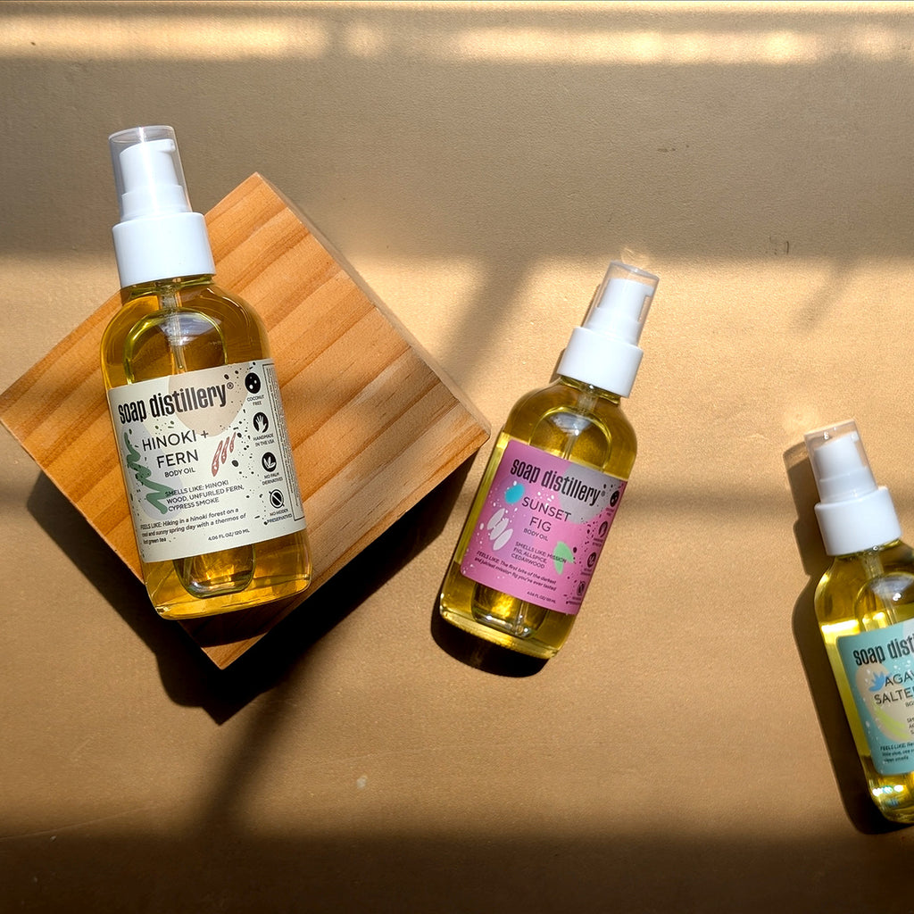 aerial view of three body oils in glass packaging with a white pump top and colorful label on the bottle